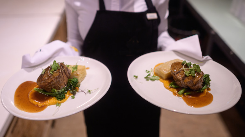 A restaurant server holding two plates of steak.