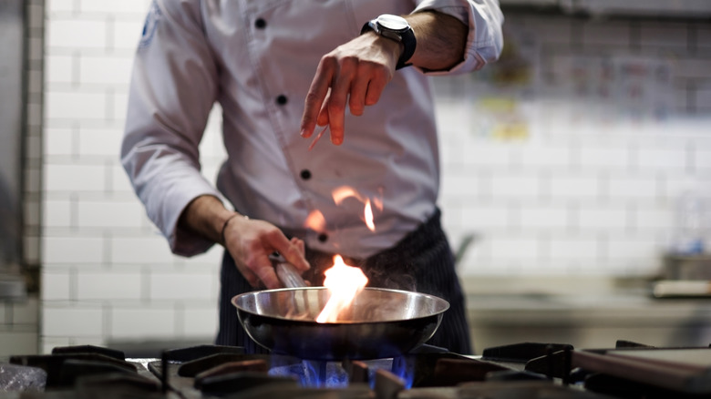 chef cooks dish with open flame on gas stovetop