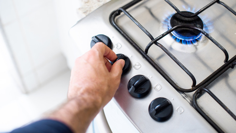 man's hand turns knob on burning gas stove