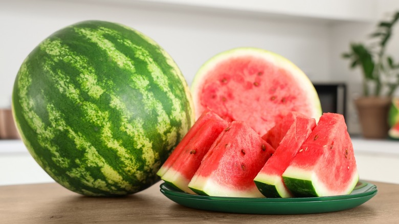 a whole watermelon, halved watermelon, and a plate of watermelon slices on a kitchen counter