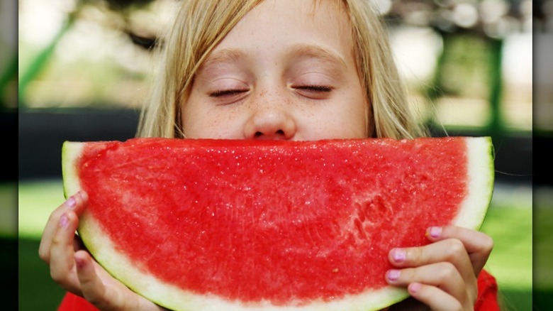 a young blond girls smells a large watermelon slice