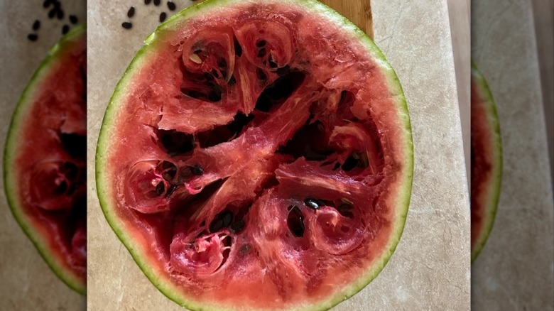 a halved watermelon with large pits and stringy flesh sits on a countertop