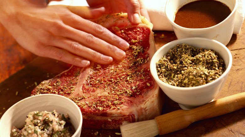 A person rubbing raw steak with herbs ready for cooking