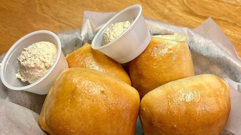 A close-up of a Texas Roadhouse rolls with plastic cups of butter