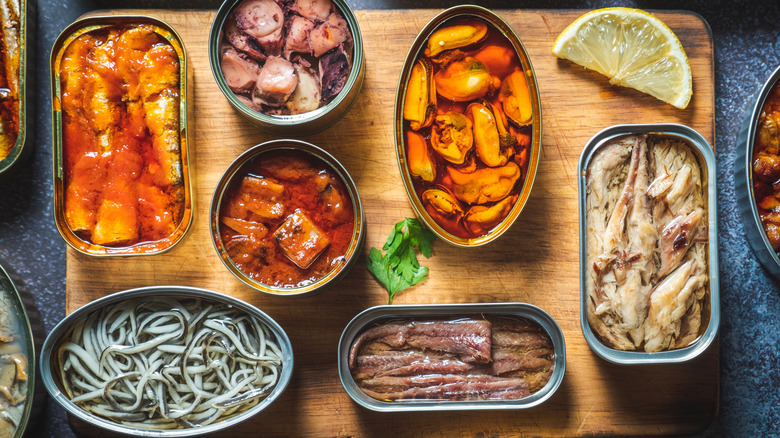 Assorted opened cans of tinned fish on wooden cutting board