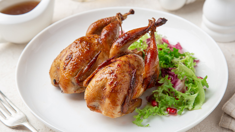 Small, whole roasted birds on a plate with a side of leafy greens.