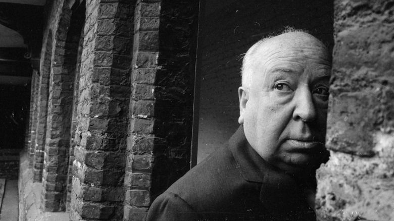 Alfred Hitchcock partially hiding behind stone wall