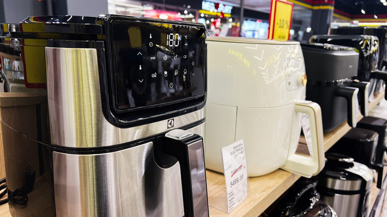 Stainless steel and white Electrolux air fryers showcased on a wooden shelf in a store.