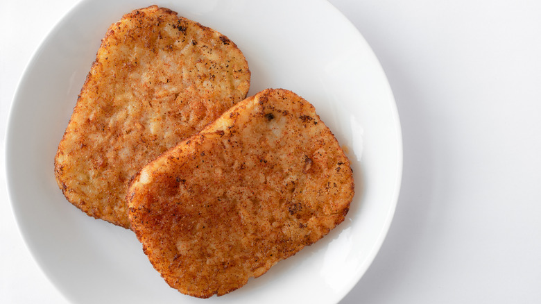 Two cooked hash browns on a white plate