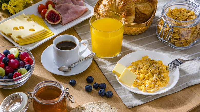 an assortment of breakfast staples, including scrambled eggs, croissants, cereal, coffee, fruits, and orange juice, on a table