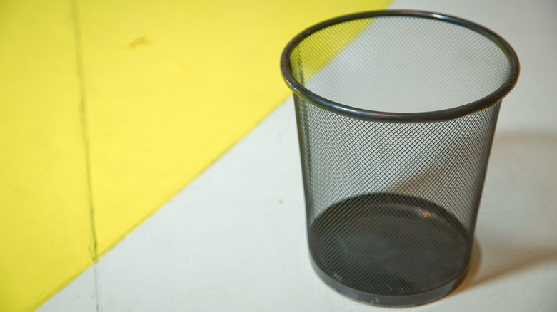 A black mesh metal trash can on a gray and yellow background