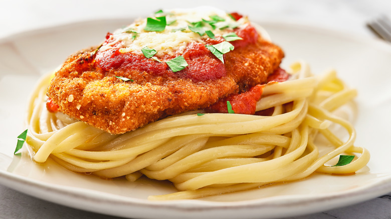 Crispy chicken parmesan on top of linguini on a white plate