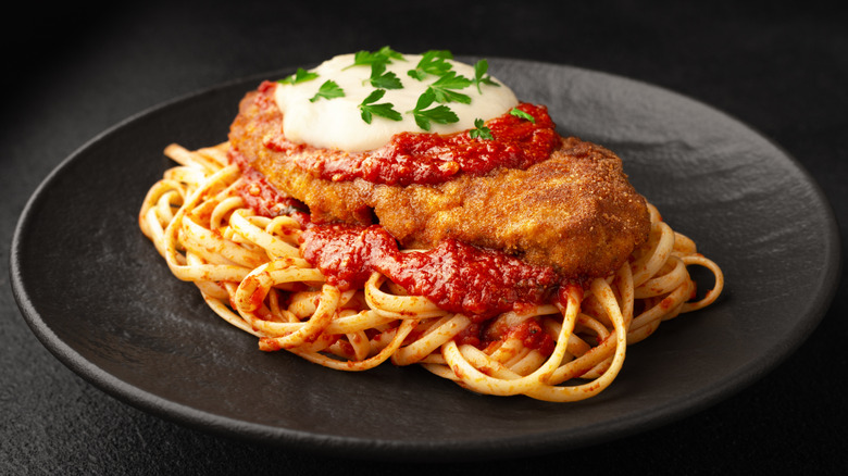 Chicken Parm on top of a bed of linguini marinara on a black plate