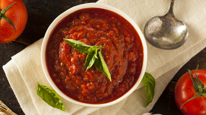 A bowl of marinara sauce with garnish and tomatoes on the side.