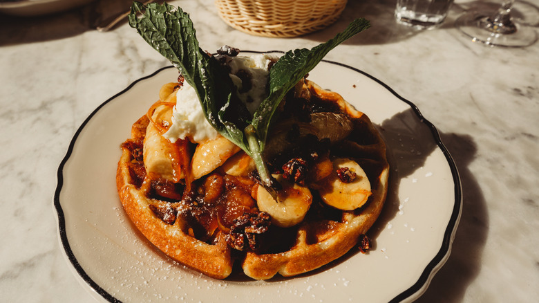 Belgian waffle with caramelized banana topping and fresh mint on a restaurant plate