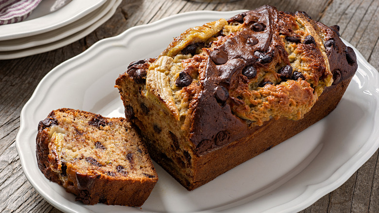 A loaf of fresh baked banana bread with chocolate chips on a white serving platter