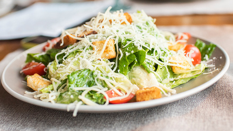 White plate topped with romaine lettuce, tomato slices, croutons, and shredded cheese at a restaurant.