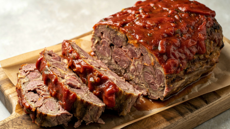 A meatloaf slathered in ketchup half-cut into pieces on a cutting board