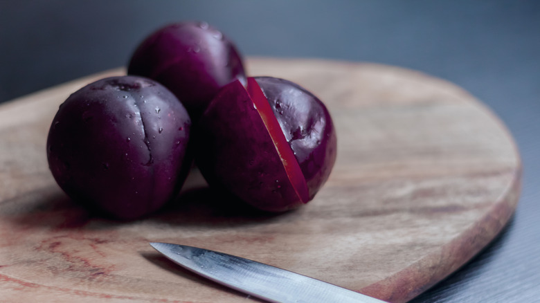 Washed plums on a wooden board with a knife