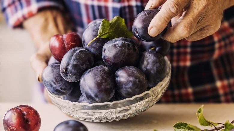 A man takes a plum from a bowl