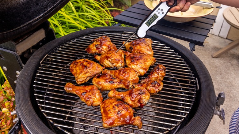Person uses a thermometer to check the temperature of chicken on a grill
