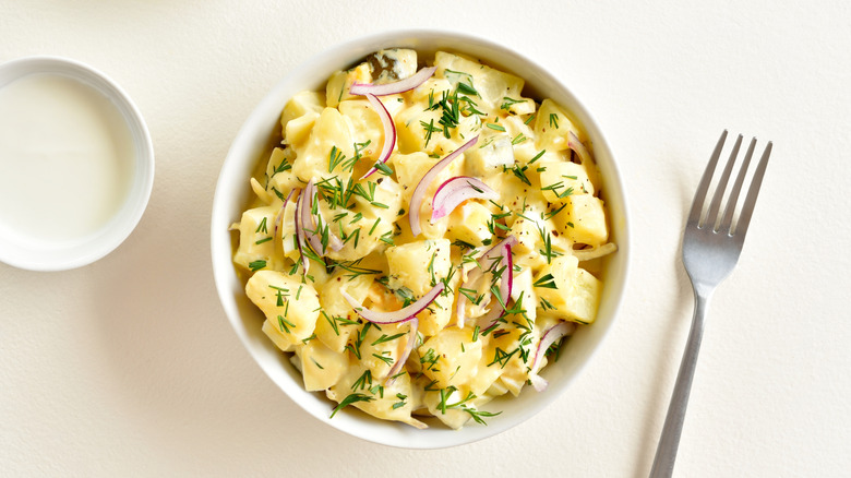 White bowl of potato salad with herbs, onions, and a fork