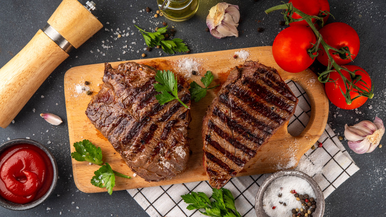 A steak served on a cutting board with ketchup and tomatoes.