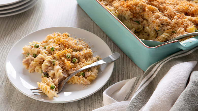 A plate of tuna noodle casserole in front of a larger square dish of the same casserole