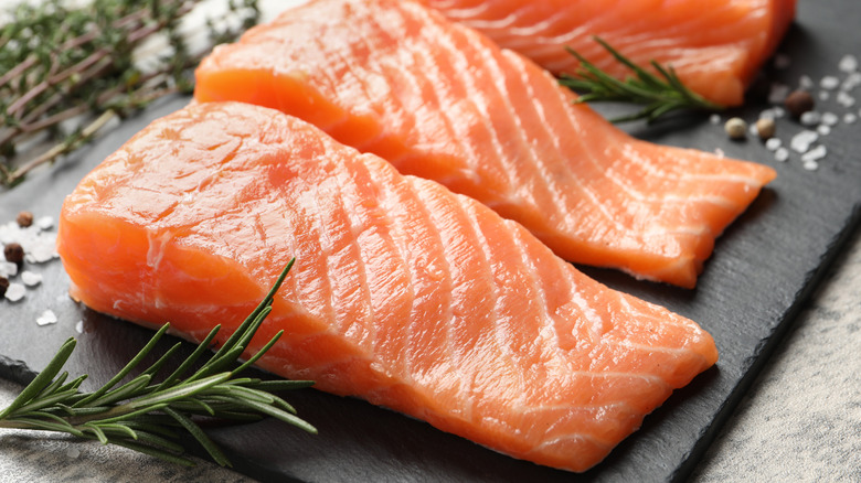Raw salmon fillets on black cutting board with rosemary sprigs