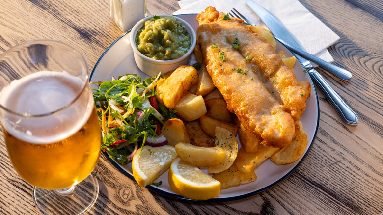 A plate with beer-battered fish, potatoes, and more with a glass of beer beside it.