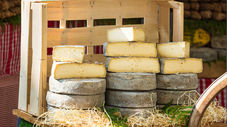 Brie cheese stacked in a rustic display with some straw, ferns and wood in the frame