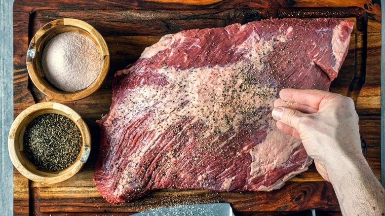 Person seasoning a beef brisket with salt and pepper
