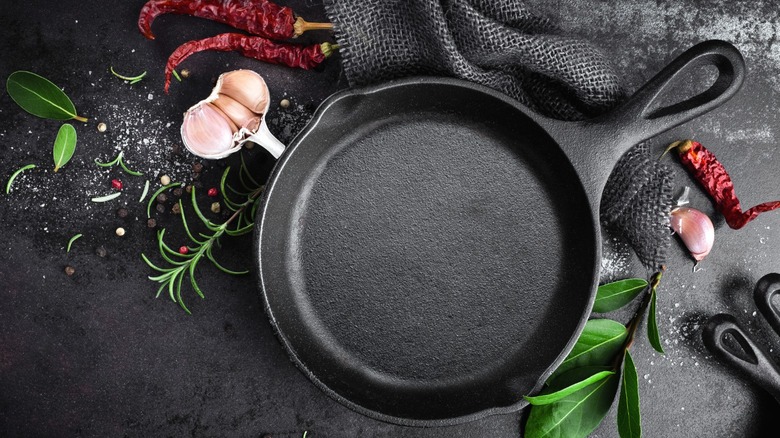 A cast iron pan on a black surface near herb springs and garlic