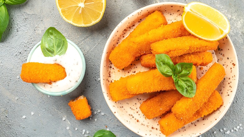 Crispy fish sticks on a plate, with one dipped in a bowl of tartar sauce.