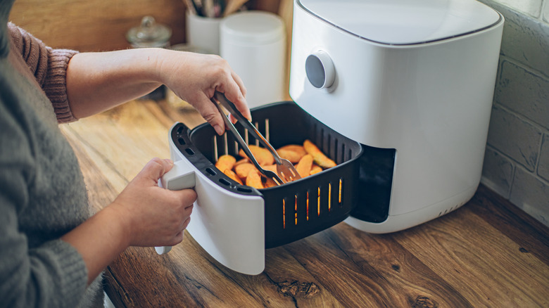Hands using tongs to flip pieces of food inside an air fryer