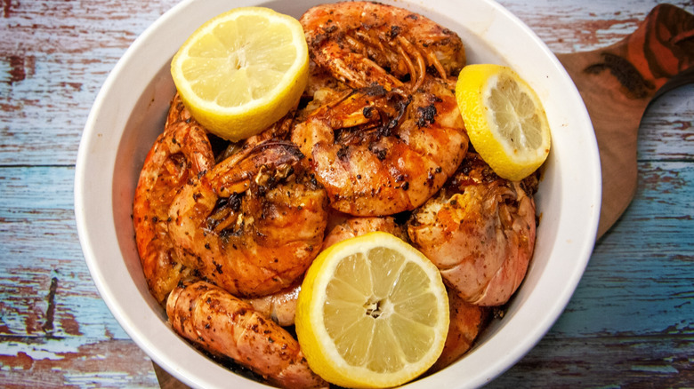 Grilled shrimp with the shells on with sliced lemon in a white bowl