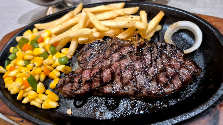 A cooked sirloin steak on a black plate alongside fries and vegetables
