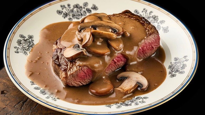 A decorative plate with a slab of steak on it covered in mushroom and sauce