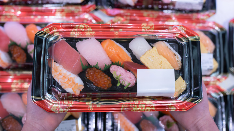 Hand holding pre-packaged sushi.