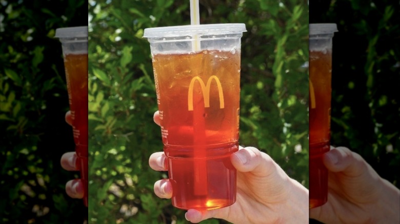 A person holds a plastic cup of McDonald's iced tea