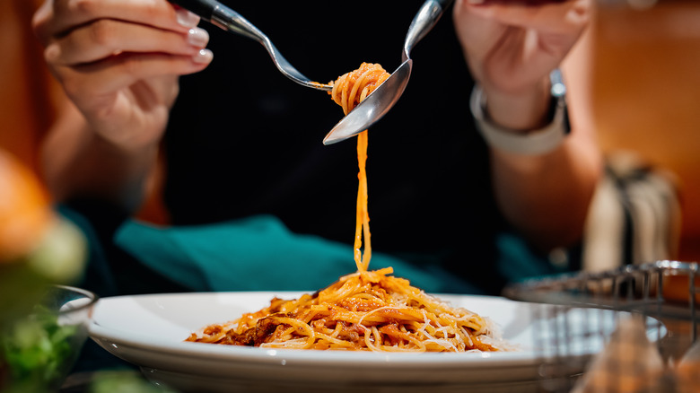 A woman twirls spaghetti onto a fork using a spoon