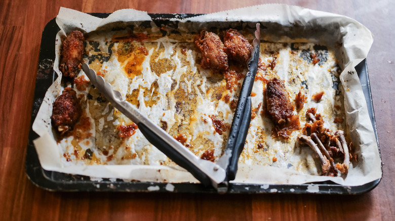 A baking tray with chicken wings and tongs