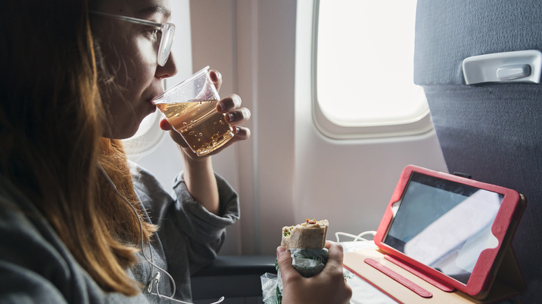 A woman drinks and eats in her seat on an airplane