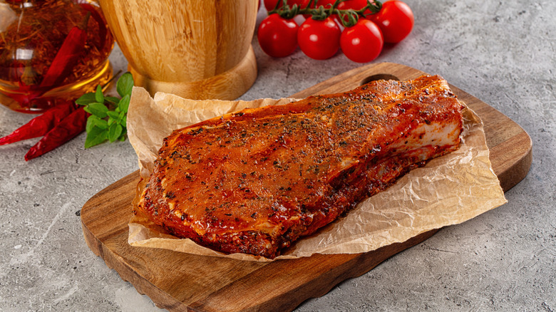 Marinated raw pork loin on a piece of paper on top of a wooden board.