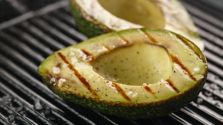 Avocado halves with grill marks and seasoning on a grill