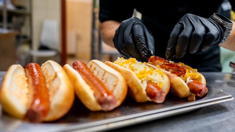 A person adding toppings to four hot dogs in buns