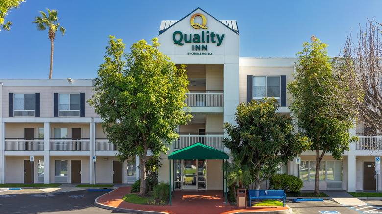 A three-story white Quality Inn with trees and balconies in front.