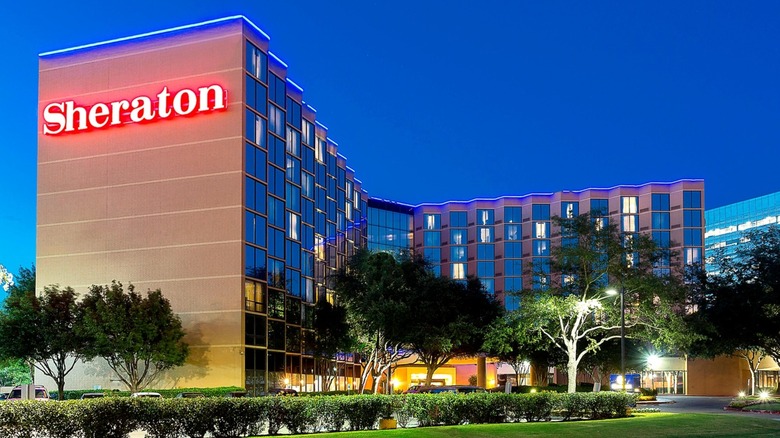 An exterior photo of Sheraton hotel with glowing red sign taken in early morning.