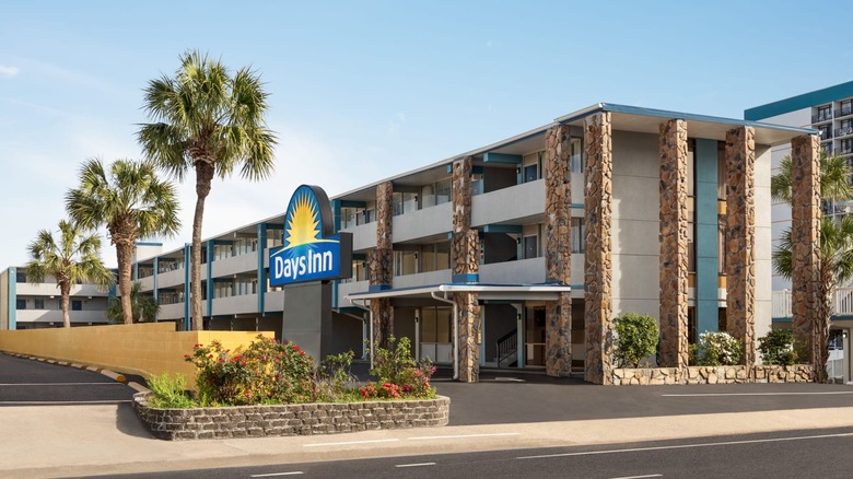 A Days Inn sign in front of a three-story hotel with stone columns and paths lined with palm trees.