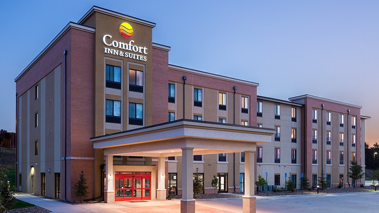The exterior of a Comfort Inn & Suites with a carport and red doors in early morning.